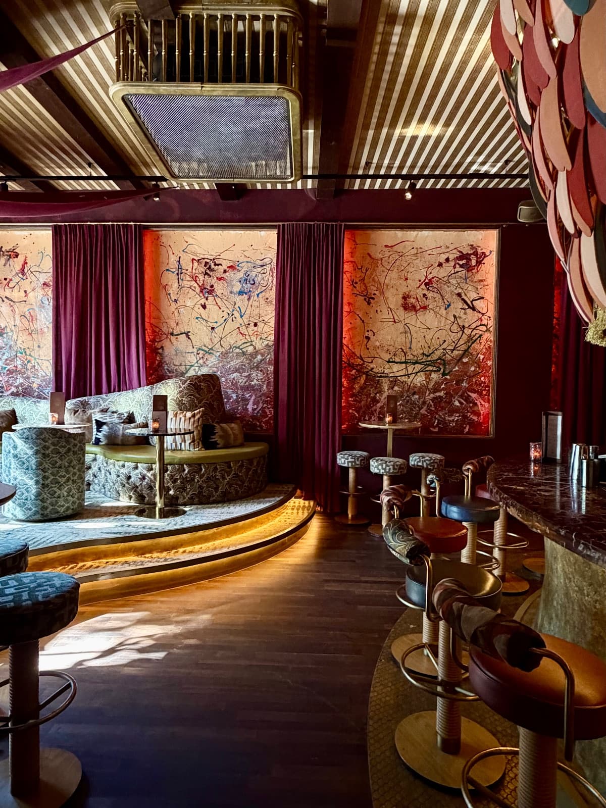 A jewel-toned Amsterdam lounge with velvet curtains, patterned banquette seating, and gallery-style splatter art