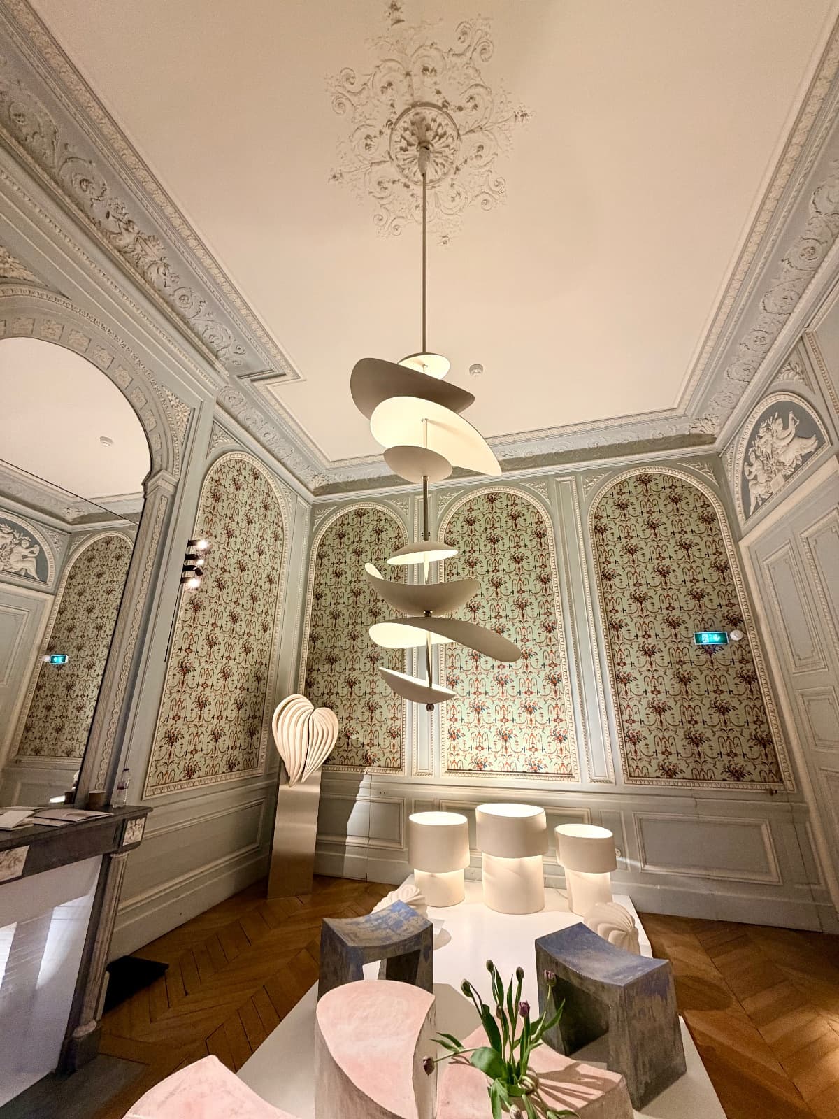 An ornate Parisian salon with patterned wallpaper and a sculptural pendant light
