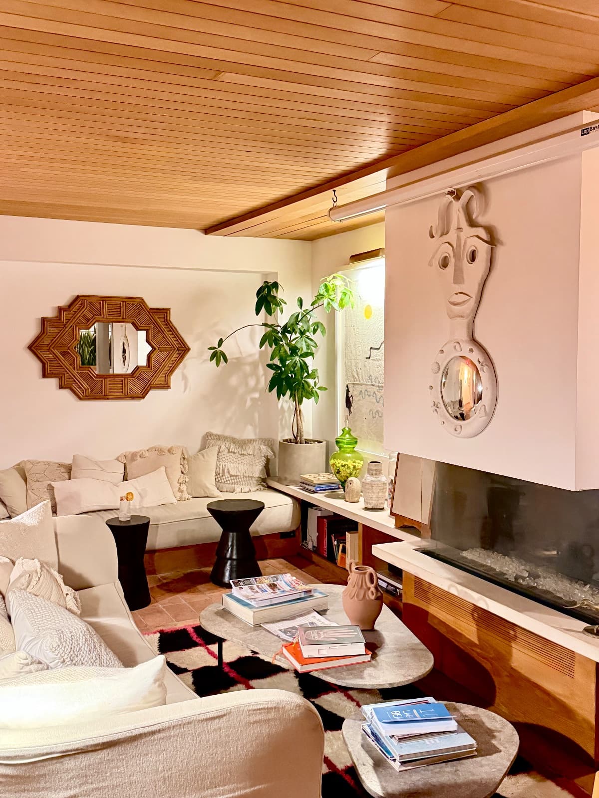 A warm living room with wood ceiling, cream sofas, and a sculptural fireplace mantel